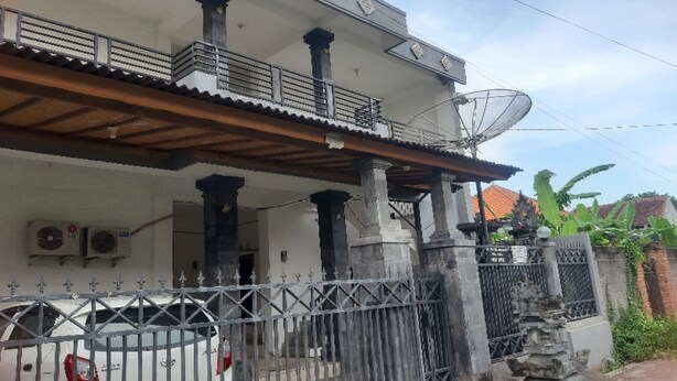 Une maison à deux étages avec un balcon, une antenne parabolique et une entrée fermée par un portail.