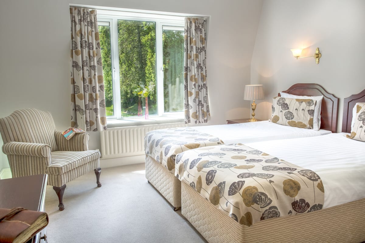 Een slaapkamer met een groot bed, een stoel, een lamp en een raam met gordijnen.