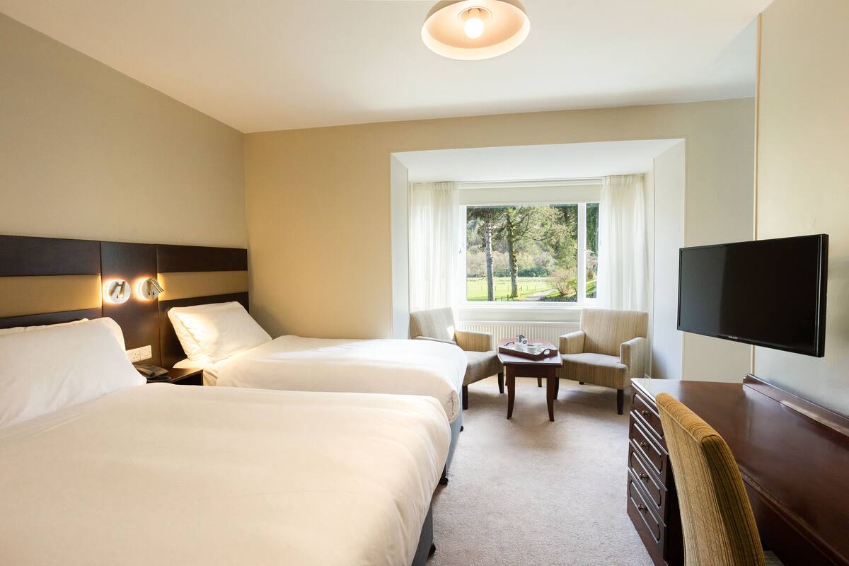 Een hotelkamer met twee bedden, een televisie, een raam met uitzicht op bomen en een stoel.