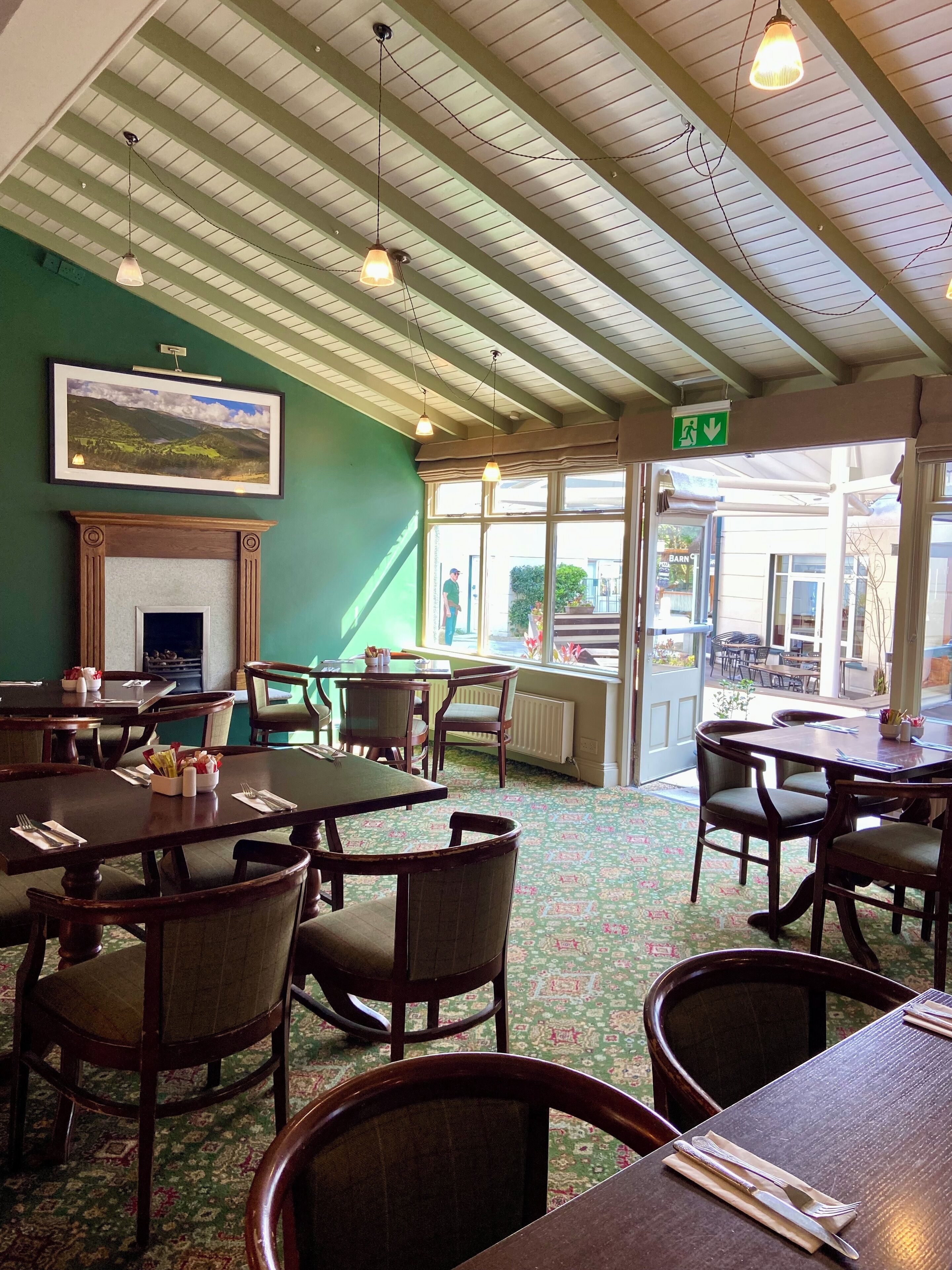 Un restaurant avec des tables et des chaises en bois, une cheminée et une vue sur l’extérieur.