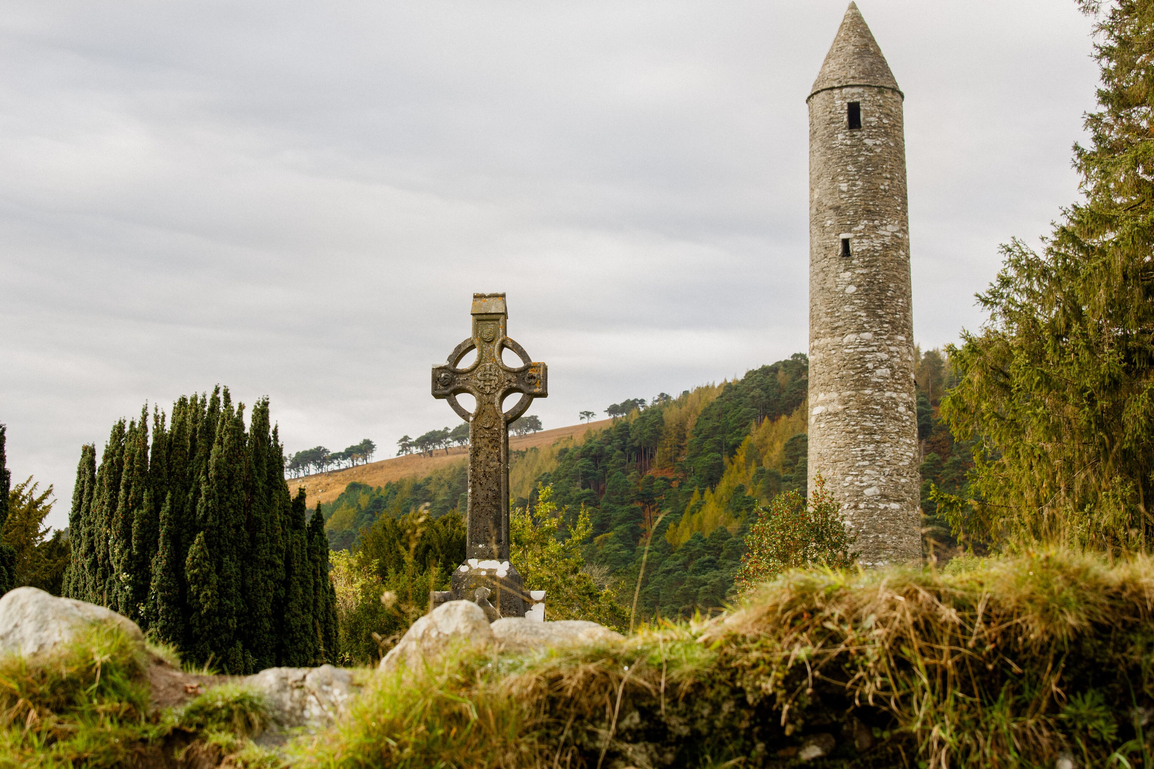 A stone tower and a cross in a grassy area with trees.