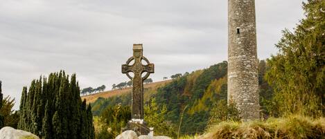 A stone tower and a cross in a grassy area with trees.