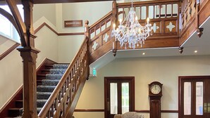 Un grand escalier orné d’un lustre, d’une horloge et de deux fauteuils à motifs dans un espace d’accueil.