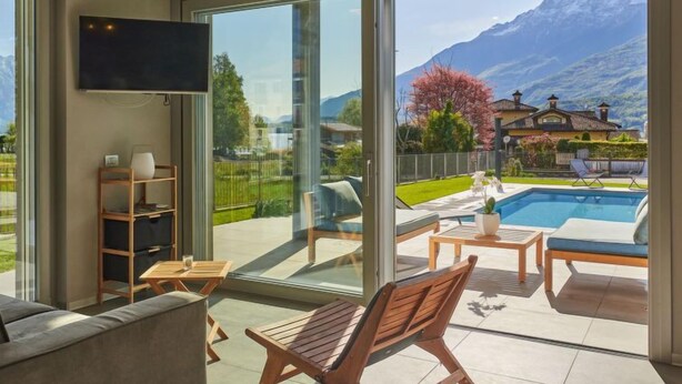 Uma sala de estar moderna com uma grande porta de vidro deslizante que dá para uma varanda com piscina e vista para as montanhas.