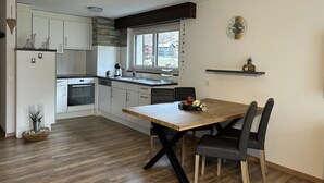 Una cocina moderna con armarios blancos, una mesa de comedor de madera y una ventana con vistas a un edificio.