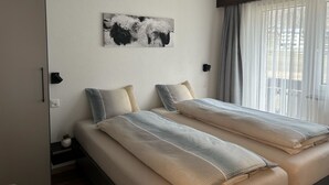 Habitación de hotel con dos camas, un cuadro abstracto grande en la pared y vistas al exterior a través de cortinas de gasa.