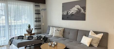 A modern living room with a grey sofa, a round wooden coffee table, and a mountain landscape painting on the wall.