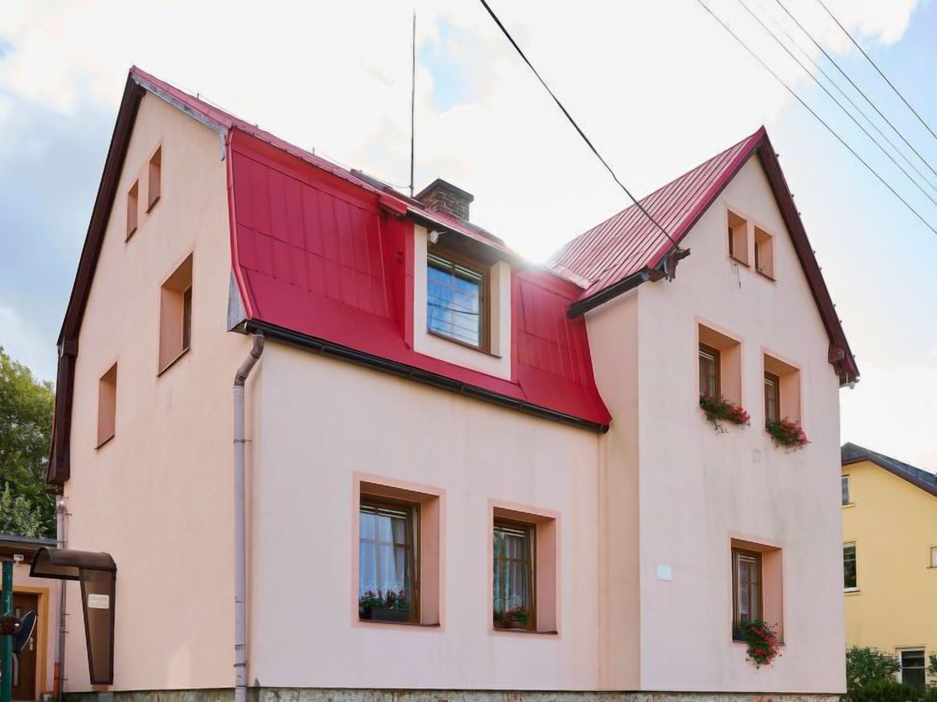 A two-story building with a red roof and beige walls, featuring multiple windows and a small balcony with flowers.