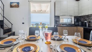 Comedor con mesa dispuesta para seis personas, vista al mar y cocina equipada con electrodomésticos modernos.