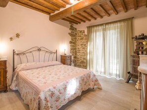 A bedroom with a bed, wooden headboard, stone wall, and a window with curtains.