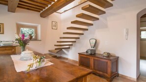 Un escalier en bois au design moderne, une table en bois ornée d’un vase de fleurs et une radio ancienne posée sur une commode en bois.