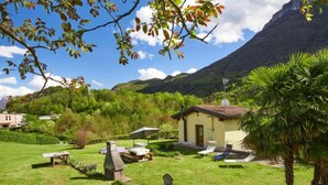 Une petite maison avec un toit rouge, entourée d’une pelouse bien entretenue et d’un jardin où poussent différentes espèces de plantes.