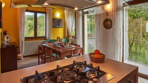 Une cuisine équipée d’une cuisinière à gaz, d’une table à manger, de chaises et offrant une vue sur la verdure environnante.