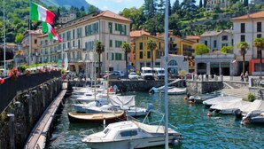 Un port de plaisance où sont amarrés des bateaux, entouré de bâtiments dotés de balcons, avec une chaîne de montagnes en arrière-plan.