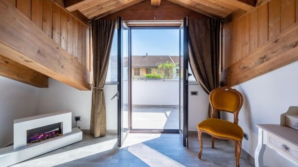Een kamer met een houten plafond, een schuifdeur naar buiten, een open haard, een gele stoel en een kleine tafel.