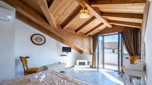 Een slaapkamer met een groot bed, houten plafond, een televisie en een schuifdeur naar buiten.
