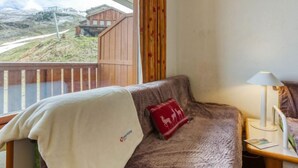 Ett mysigt rum med en soffa, ett litet bord med en lampa och utsikt över en träbyggnad och en väg utanför.