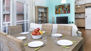 Een eetruimte met een tafel voor vier personen, een schaal fruit en een televisie op de achtergrond.