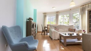 Een woonkamer met een blauwe fauteuil, een witte bank, een houten salontafel en een eethoek met een tafel en stoelen.