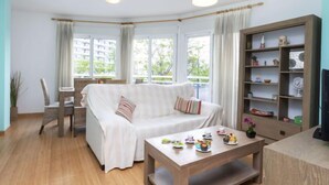 Een gezellige woonkamer met een bank, een bijzettafeltje met decoratieve objecten, een boekenkast en een eethoek met stoelen en een tafel.