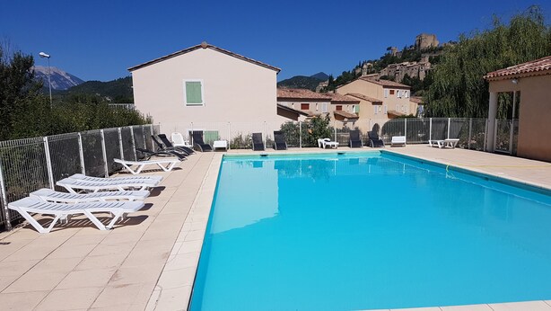 En pool med solstolar, en liten byggnad och en bergig bakgrund.