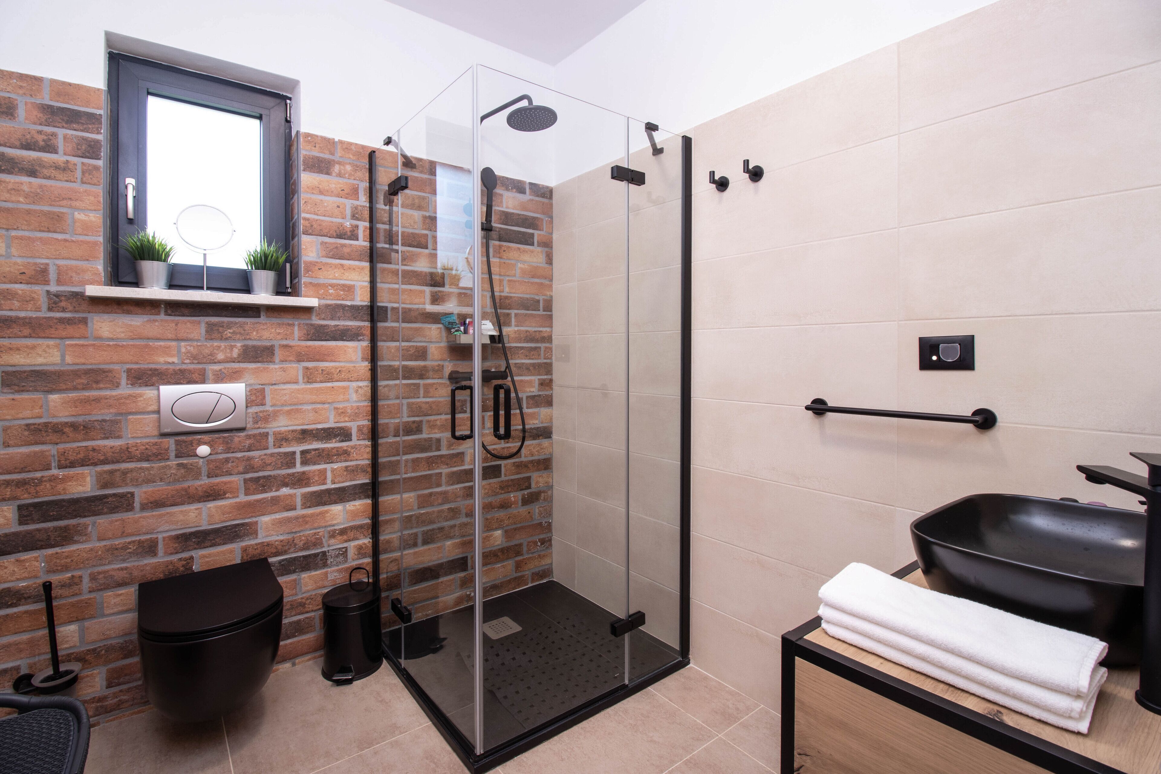 A modern bathroom with a glass-enclosed shower, a black sink, and a wooden vanity.