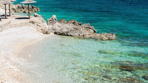 A beach with clear turquoise water, rocky formations, and a few umbrellas.
