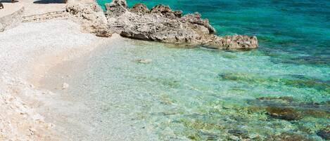 A beach with clear turquoise water, rocky formations, and a few umbrellas.