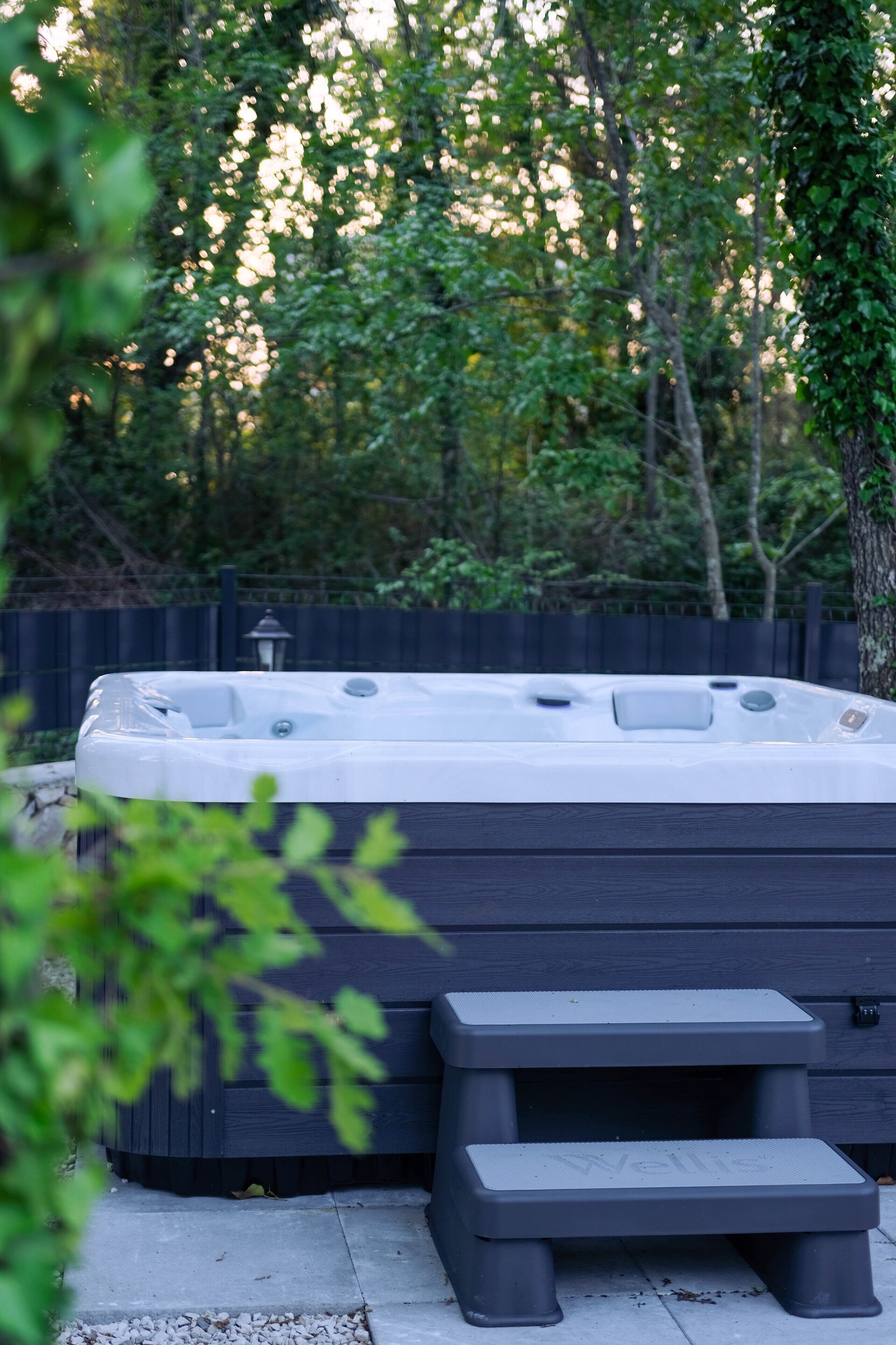 Un bain à remous avec des marches, entouré d’une clôture en bois et d’arbres.