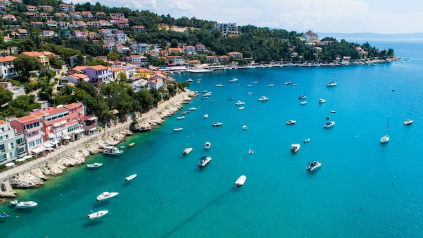 A coastal town with a marina filled with boats, colorful buildings along the shore, and a hilly backdrop.