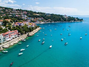 Un pueblo costero con un puerto deportivo lleno de barcos, edificios coloridos a lo largo de la costa y un paisaje montañoso al fondo.