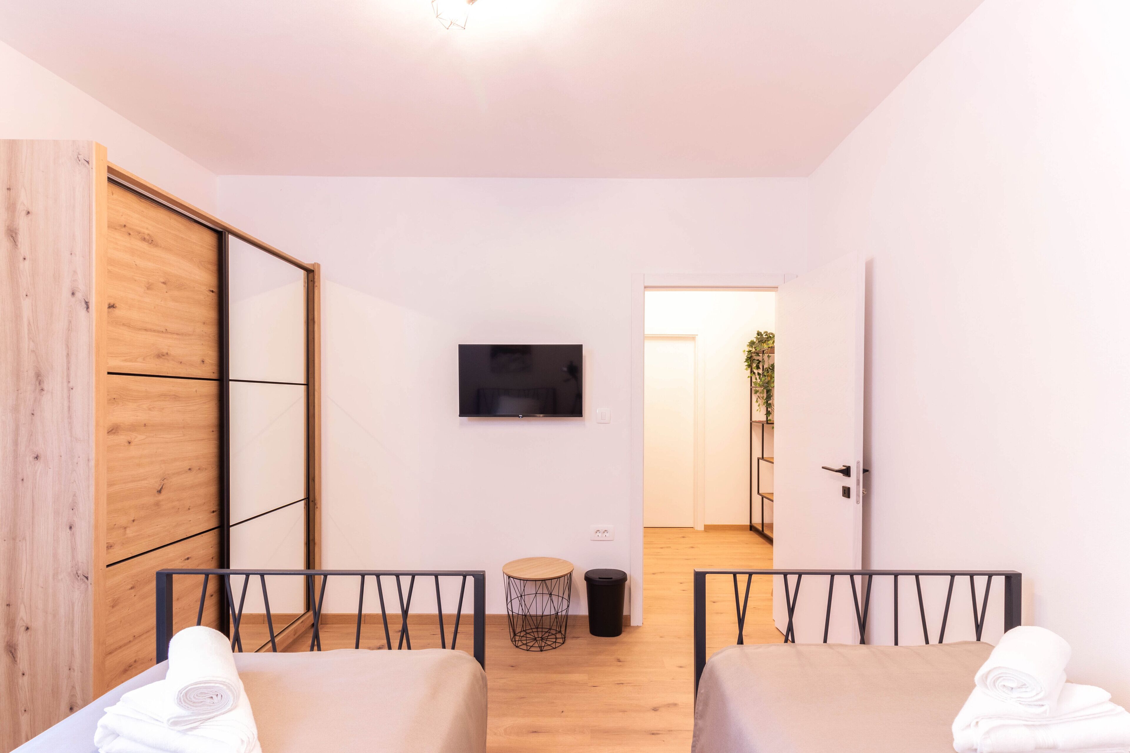 Ett modernt hotellrum med en garderob i trä, en platt-TV, ett litet runt bord och två sängar med prydligt hopvikta handdukar.