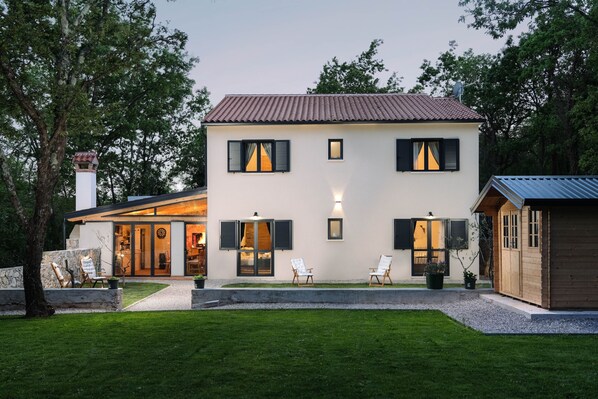 A two-story house with a white exterior, black shutters, and a tiled roof. There are two chairs outside and a small wooden structure to the right. -  VILLA PORTUM - Serenity, Nature, Heated Pool, FAMILY ONLY (Labin)