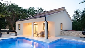 A modern house with a swimming pool, outdoor seating, and a stone wall.