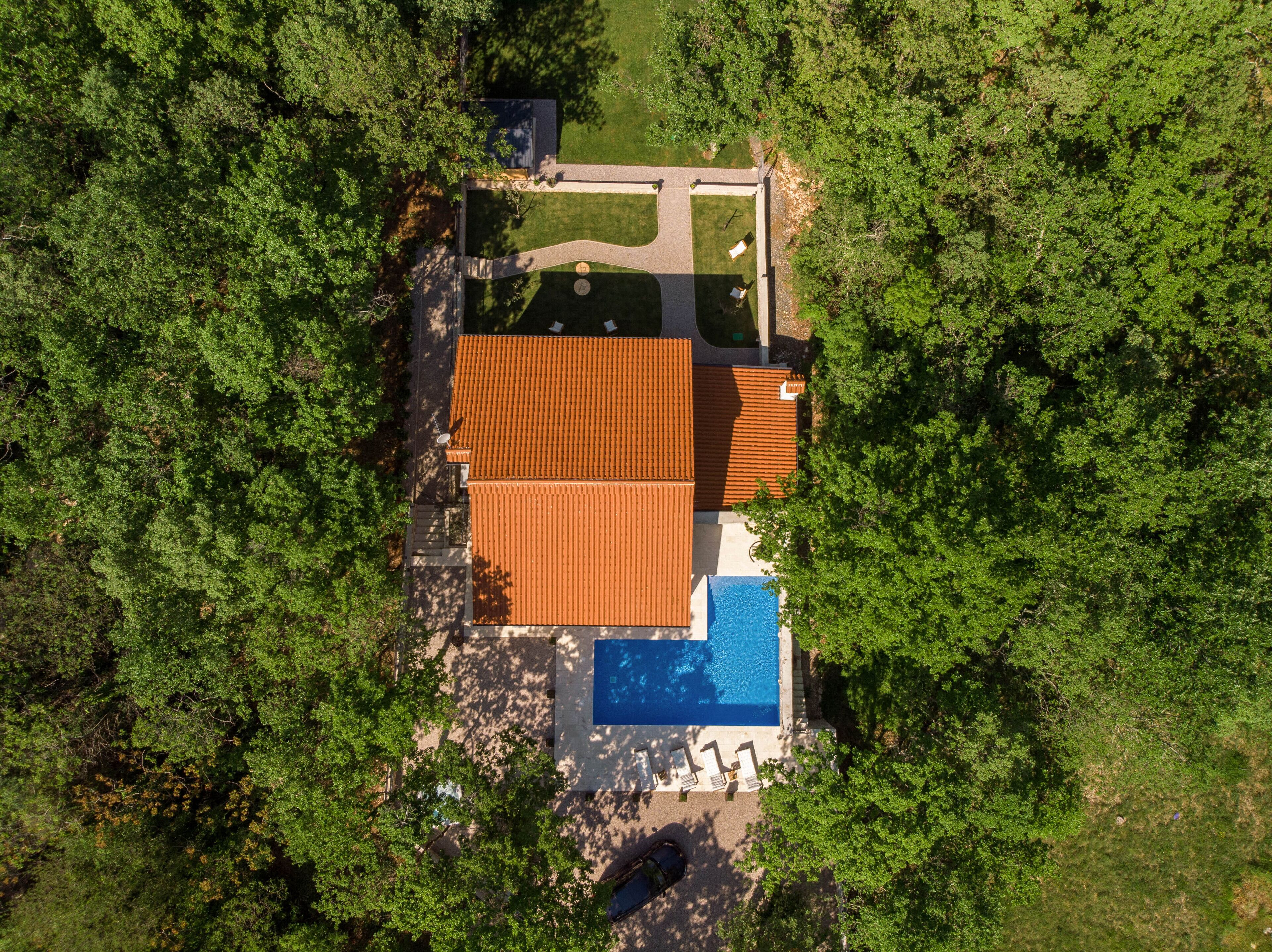 An aerial view of a house with a swimming pool, surrounded by dense greenery.
