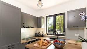 A modern kitchen with grey cabinets, a wooden countertop, and a window with a view of greenery.