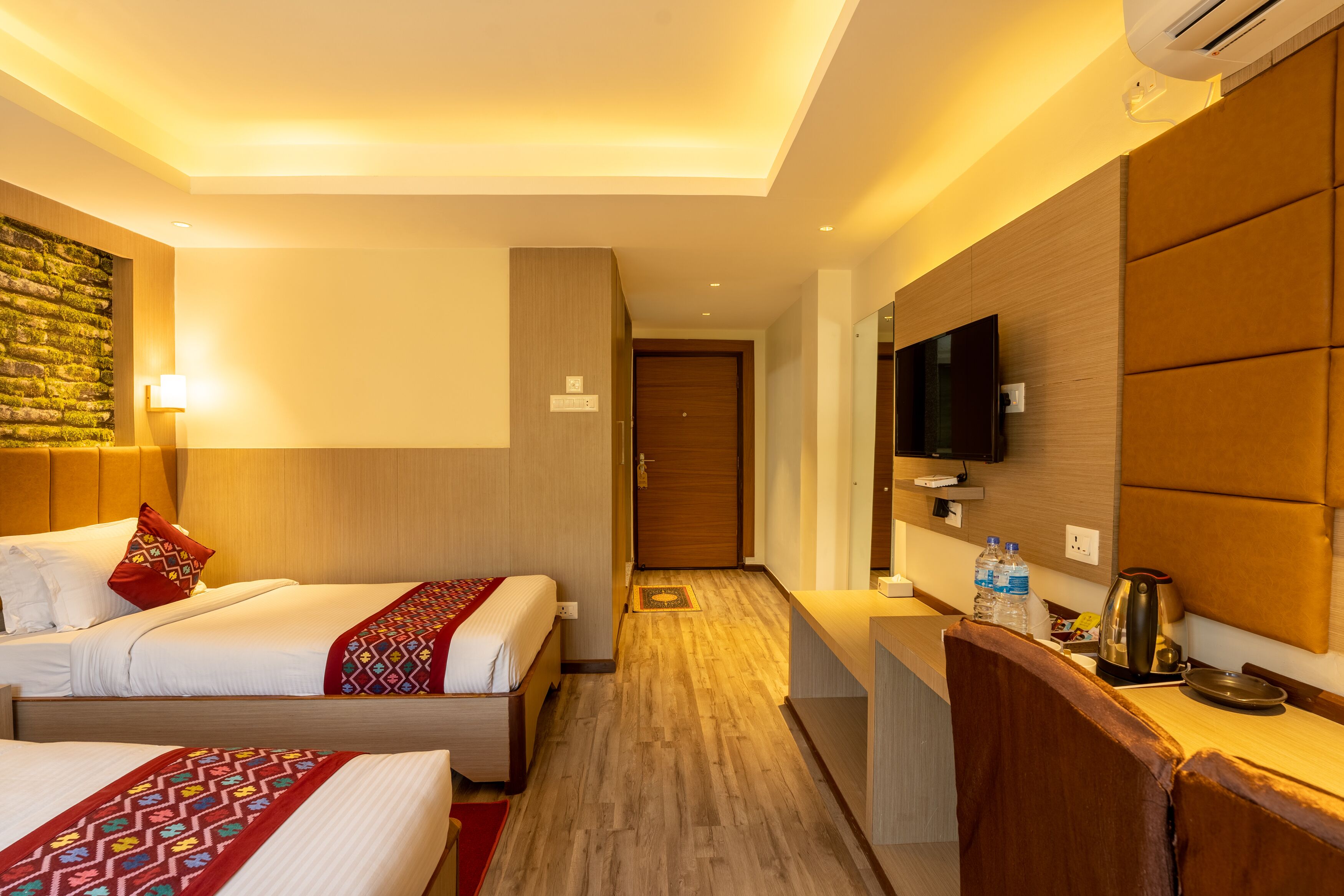 A hotel room with two beds, a wooden headboard, a flat-screen TV, a coffee maker, and a small kitchenette.