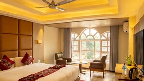 Une chambre d’hôtel avec un grand lit, un ventilateur de plafond, une fenêtre avec des rideaux, une petite table et une chaise.