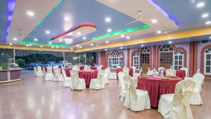 Une salle de banquet avec des tables rondes recouvertes de nappes rouges, des chaises blanches ornées de nœuds et un plancher en bois.
