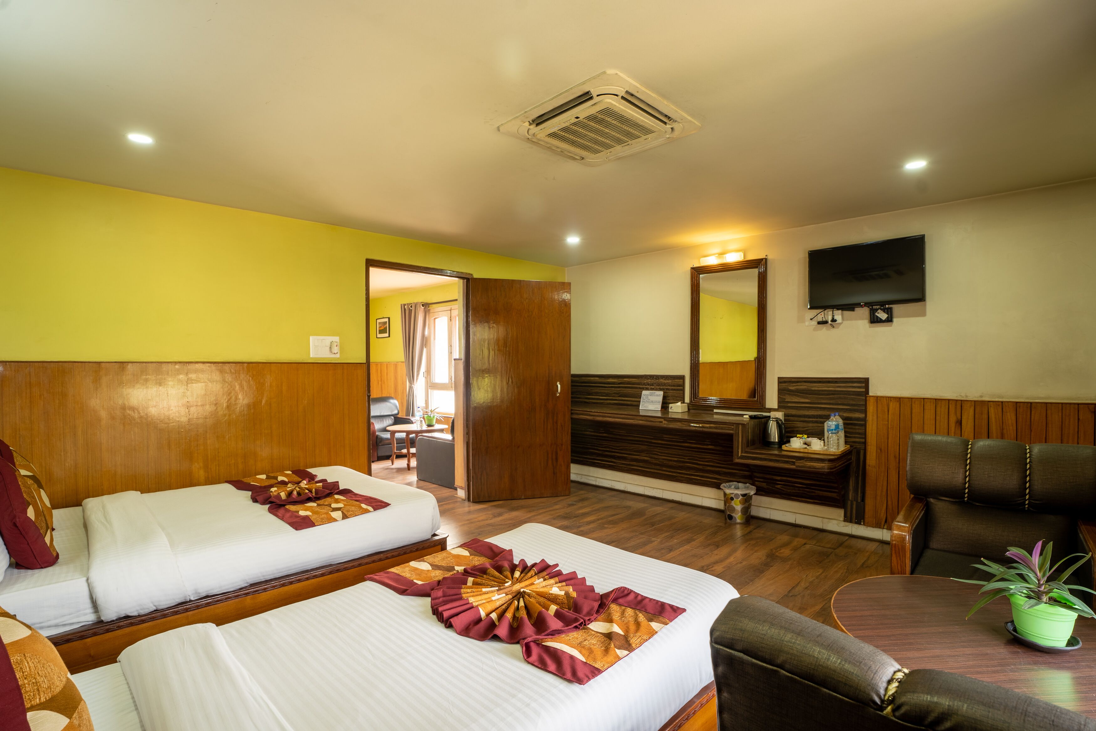 A hotel room with two beds, a desk, a chair, a TV, and a reception area.