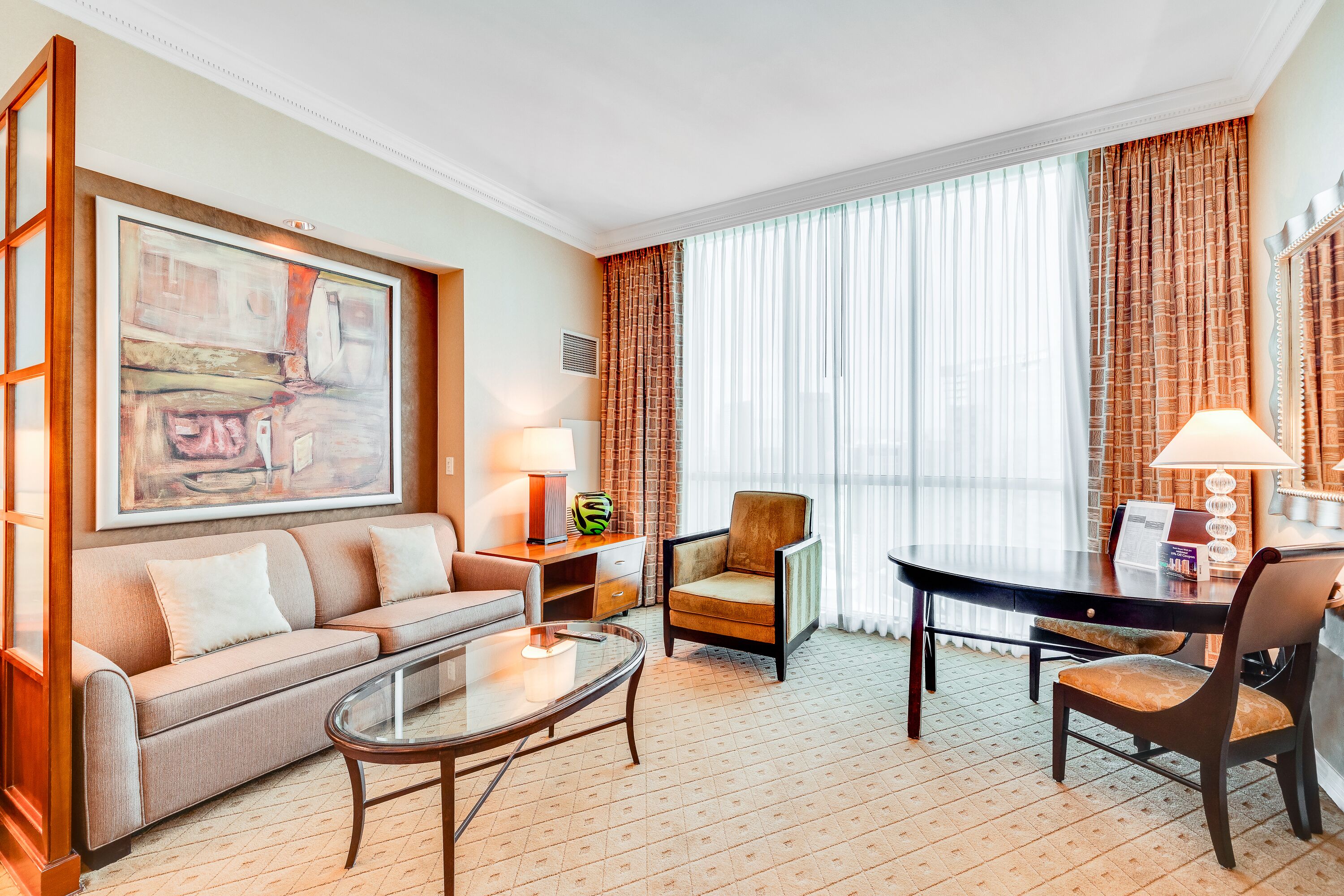 Une chambre d’hôtel avec un canapé, un fauteuil, une table à manger et un grand tableau au mur.