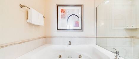 A bathroom with a large bathtub, a framed artwork above the sink, and a towel rack on the wall.