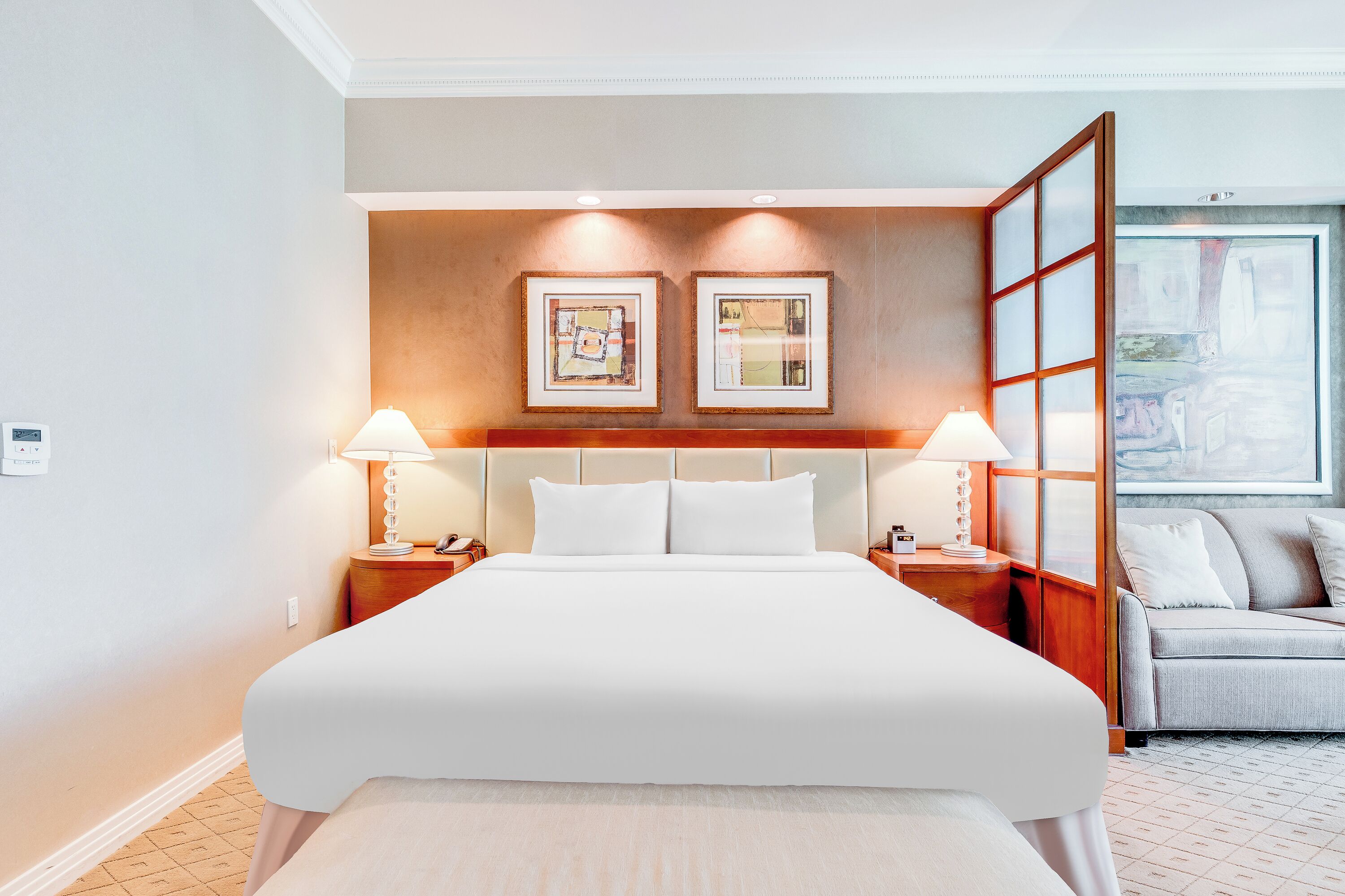 A hotel room with a large bed, two bedside lamps, a wooden headboard, and two framed pictures on the wall.