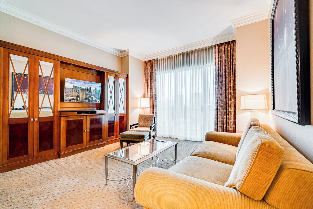 A hotel room with a large flat-screen TV, a sofa, a coffee table, and a cabinet with a mirror.