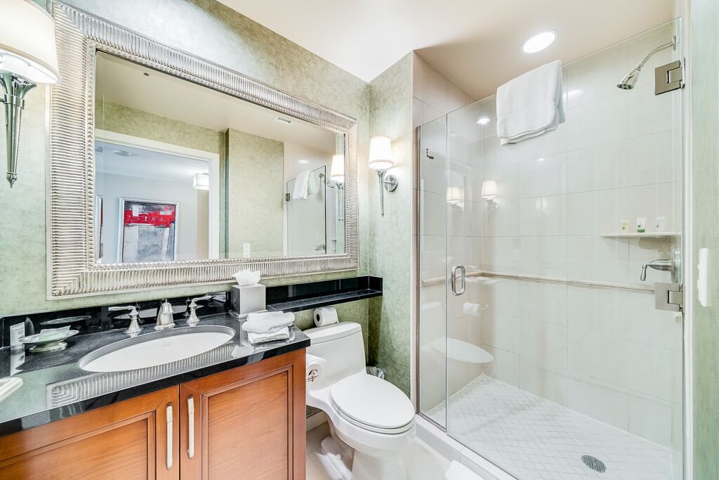 A modern bathroom with a large mirror, two sinks, a toilet, and a walk-in shower.