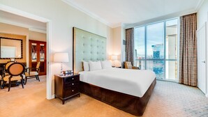 Ein Hotelzimmer mit einem großen Bett, einem Nachttisch, einem Schreibtisch mit Stuhl und Blick auf die Stadt durch große Fenster.