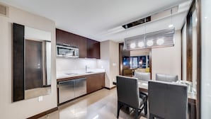 A modern kitchen with a dining area, featuring stainless steel appliances, wooden cabinets, and a contemporary light fixture. - Vdara Studio by Jet Luxury (Las Vegas)