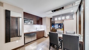 A modern kitchen with a dining area, featuring stainless steel appliances, wooden cabinets, and a contemporary light fixture. - Vdara Adjoining Parlor Suite by Jet Luxury (Las Vegas)