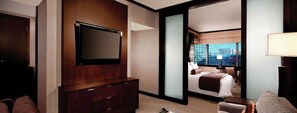 Une chambre d’hôtel dotée d’un grand téléviseur  à écran plat fixé à un meuble en bois, d’un lit offrant une vue sur la ville et d’un bureau avec une lampe.