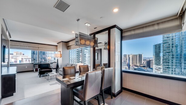 Una habitación de hotel moderna con zona de comedor, ventanas amplias con vistas a la ciudad y una kitchenette.